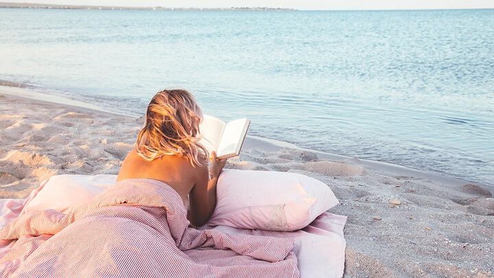 Topless woman reading a book on a mattress on the beach